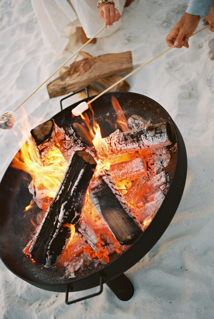 A really lit bonfire with coals and a really bright fire. There's people out of focus around it.